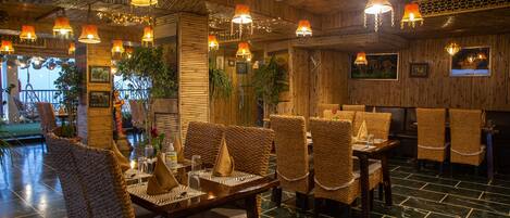 A restaurant with wicker chairs, wooden tables, and hanging lights.