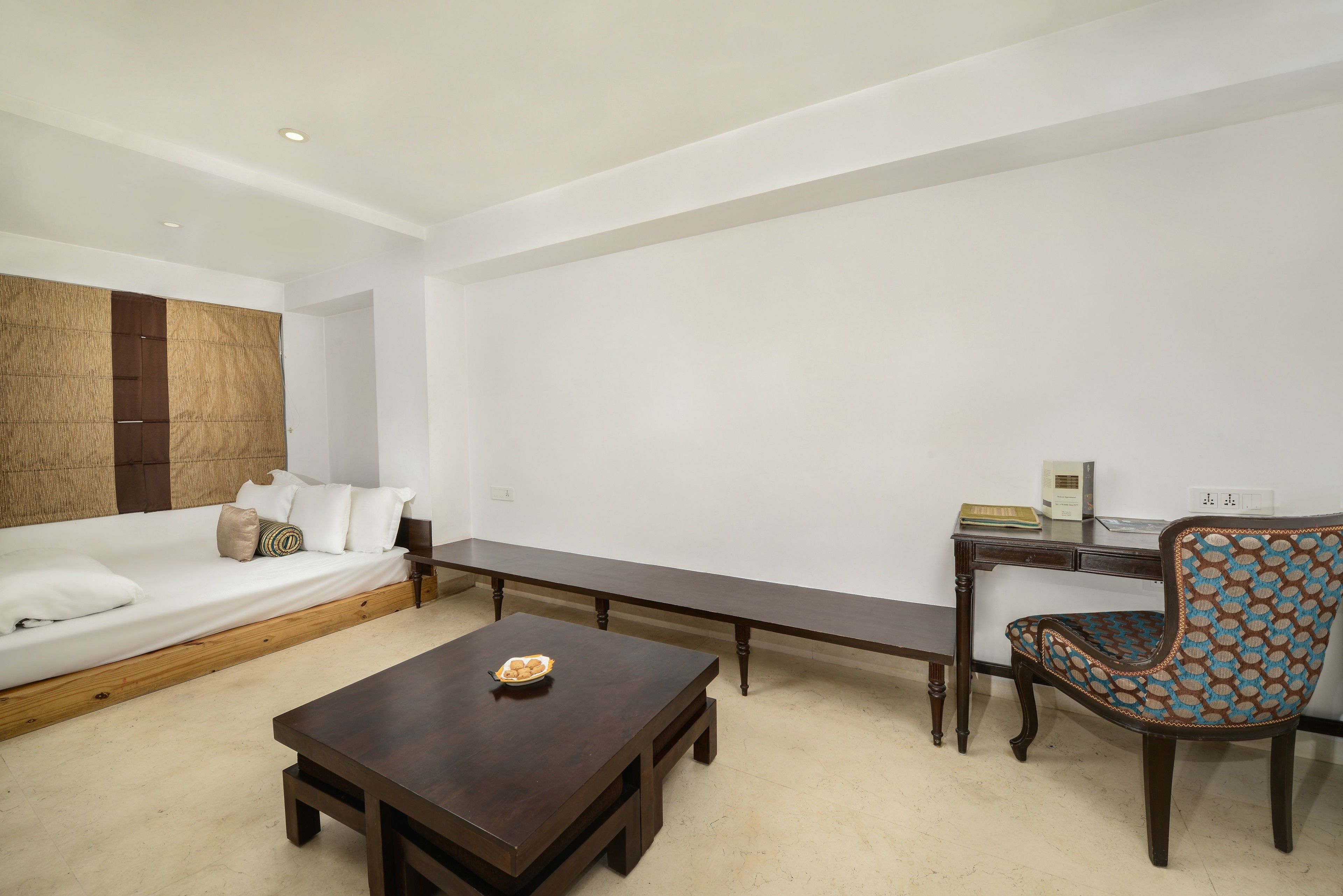 Una habitación moderna con una cama, una mesa de centro de madera, un sillón estampado y un escritorio con lámpara.