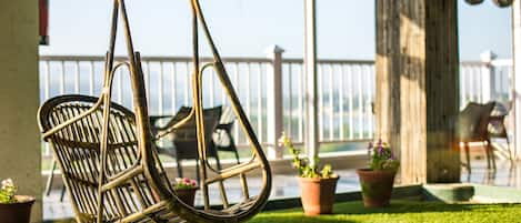 A wicker chair hanging on a balcony with a view of the sea and potted plants.
