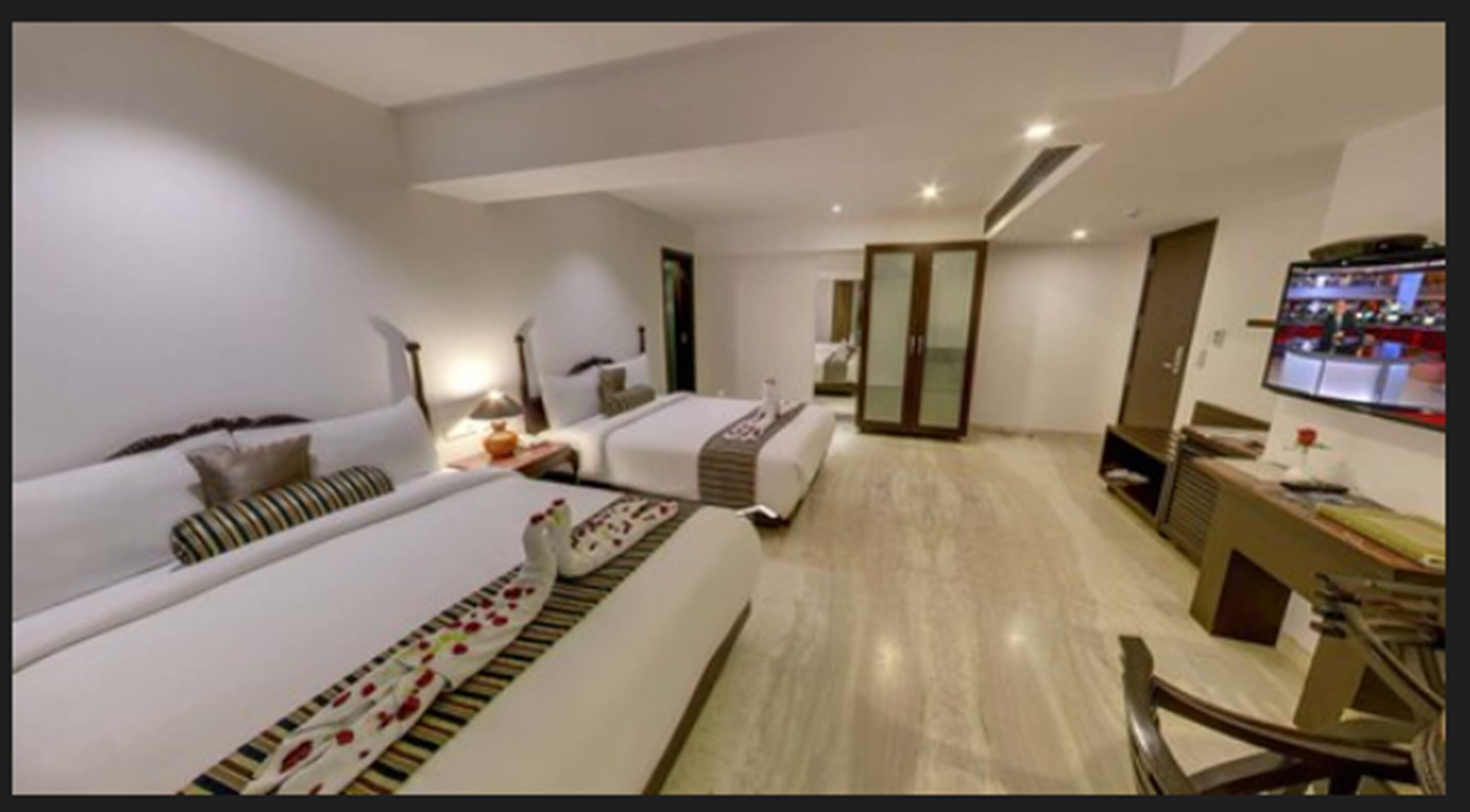 A hotel room with two beds, a desk, a TV, and a wardrobe.