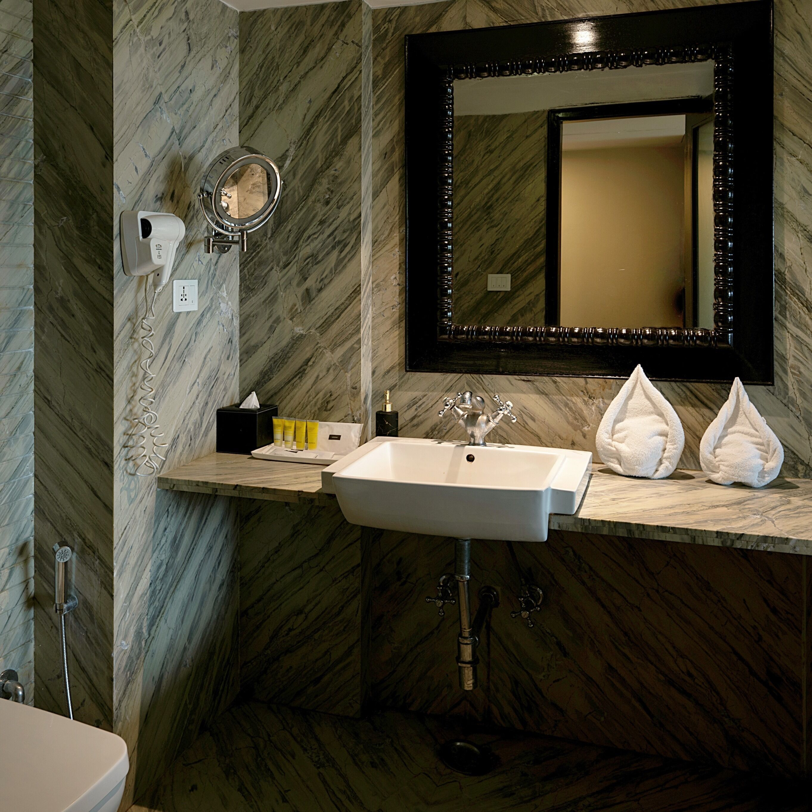 A bathroom with a marble wall, a sink with a mirror, and a towel dispenser.
