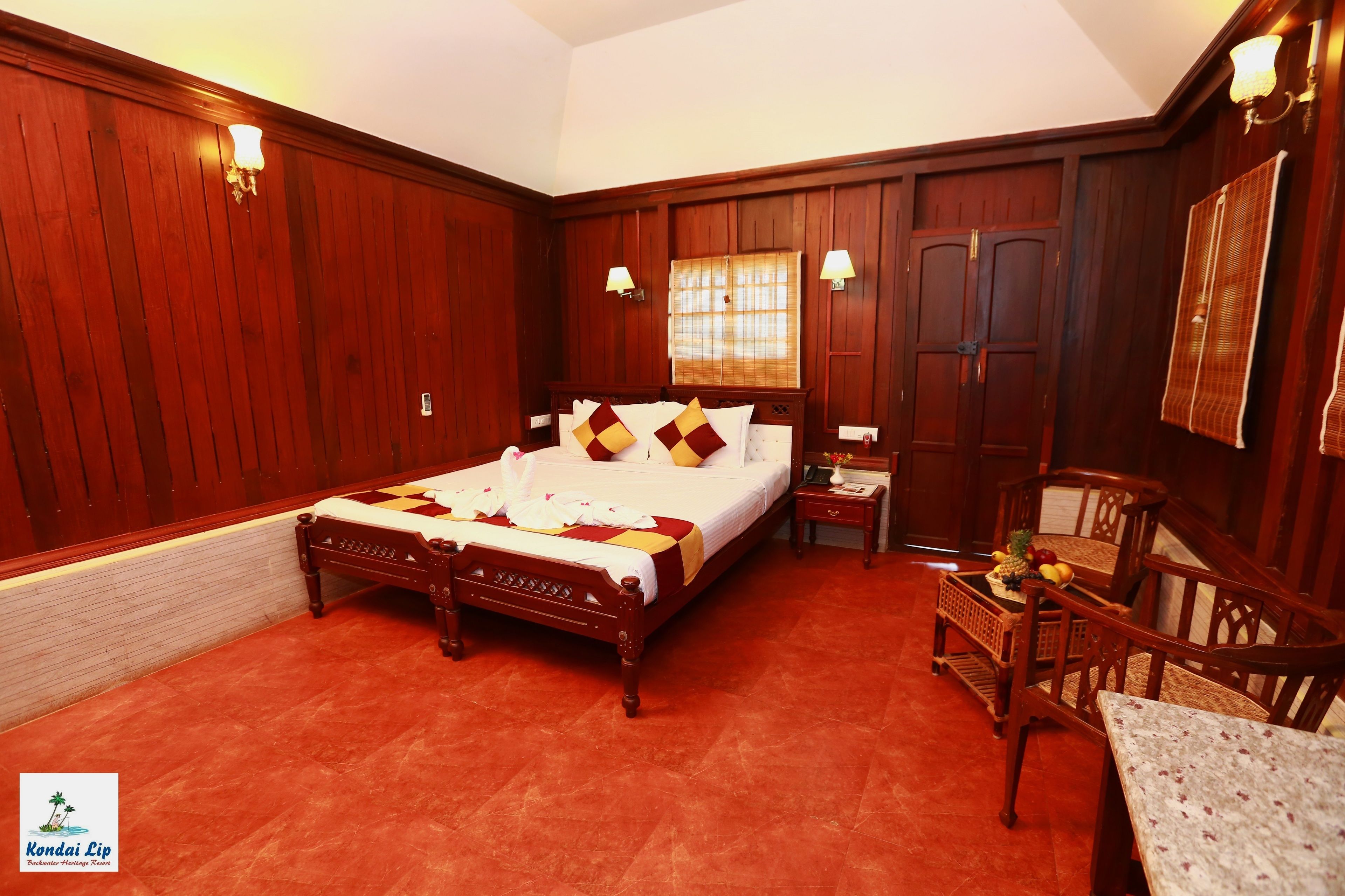 A hotel room with a large bed, wooden walls, a small table with fruit, and a chair.