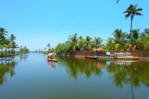 Un río tranquilo con barcos, palmeras y un letrero que dice 'Kondai Lip Backwater Heritage Resort'.