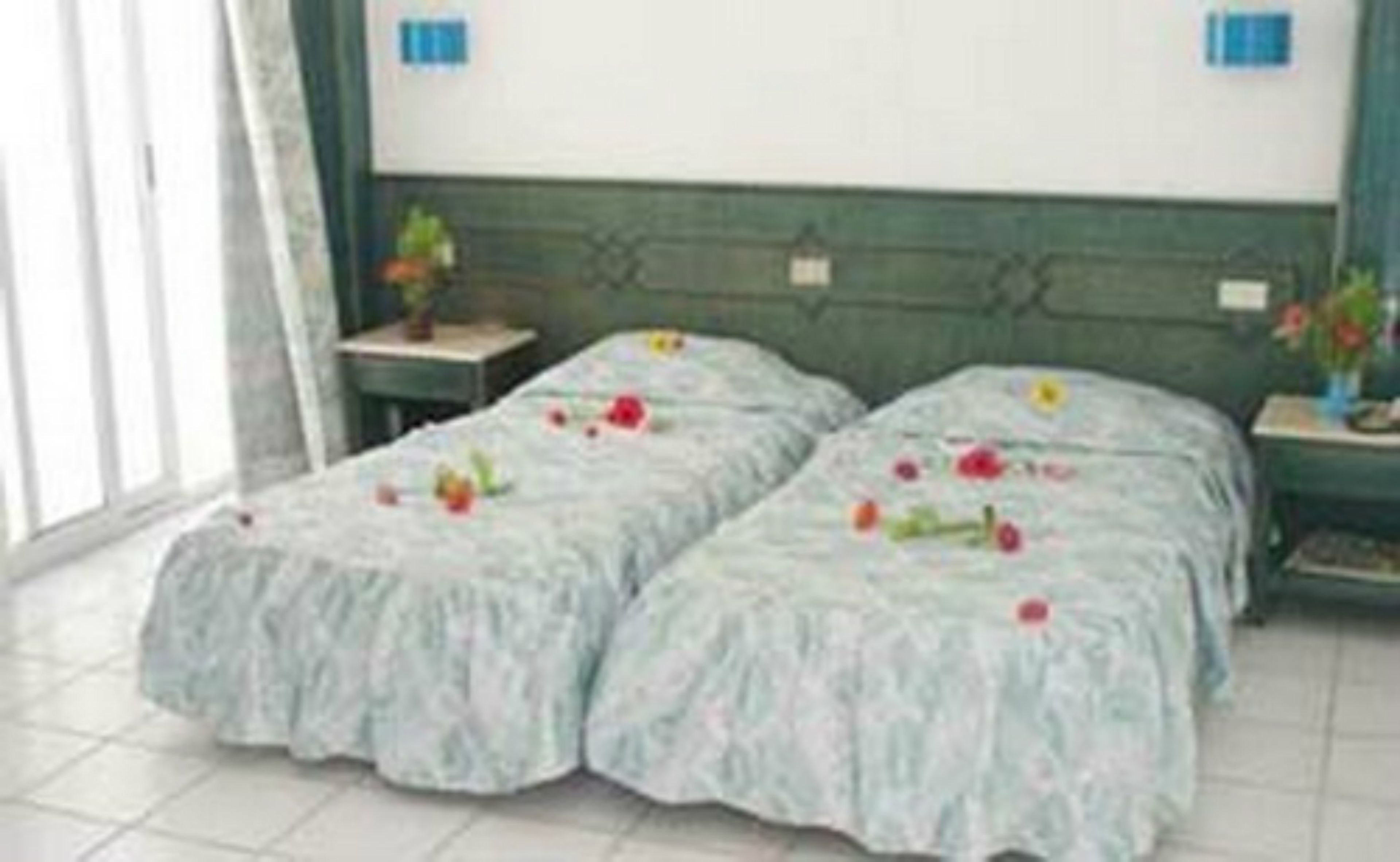 Una habitación con dos camas, cada una con una colcha estampada con motivos florales, cabeceros verdes y mesitas de noche con lámparas.