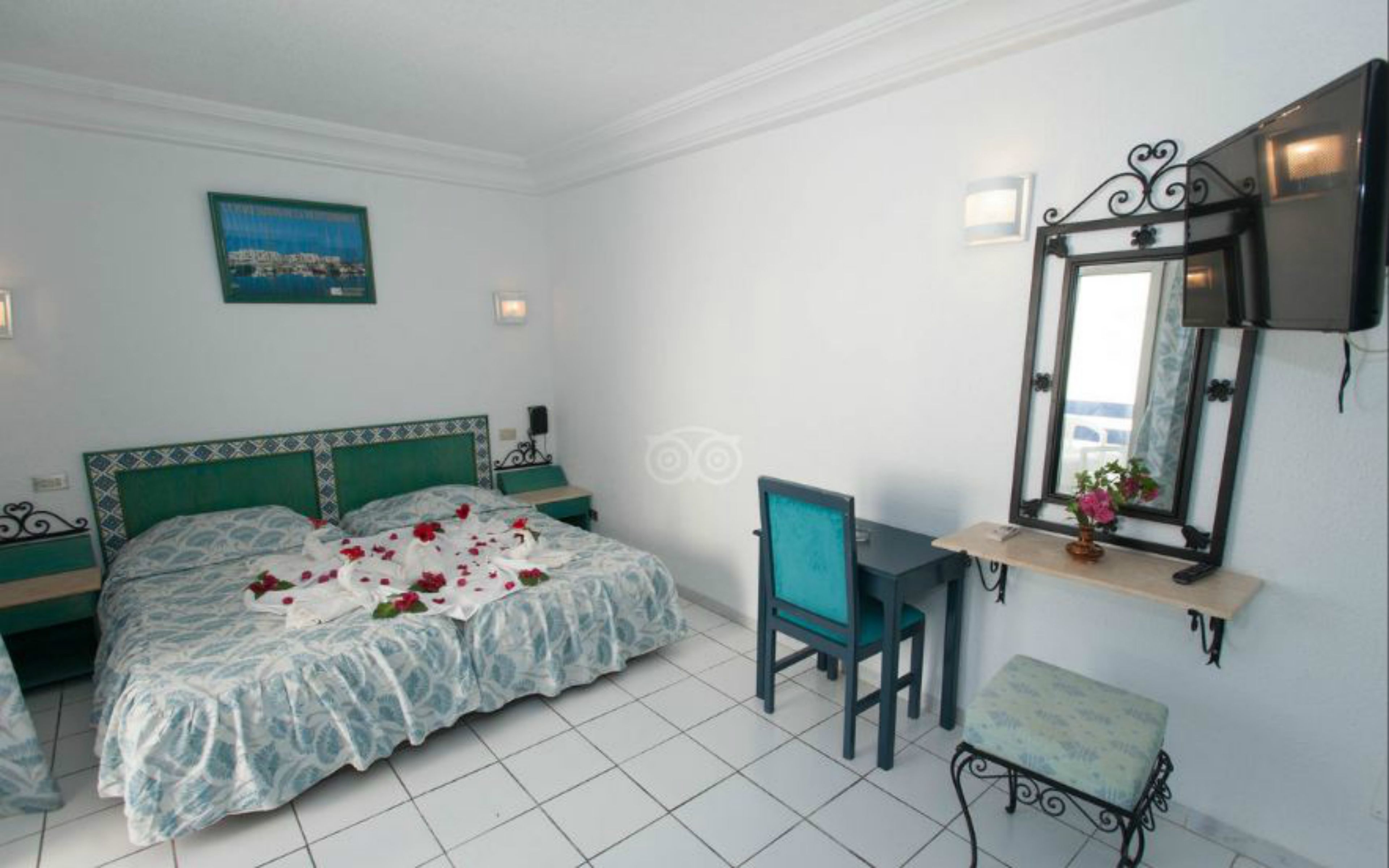 A bedroom with a bed, a desk, a chair, a bench, a mirror, and a picture on the wall.