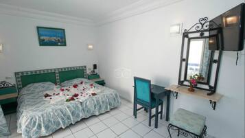 A bedroom with a bed, a desk, a chair, a bench, a mirror, and a picture on the wall.