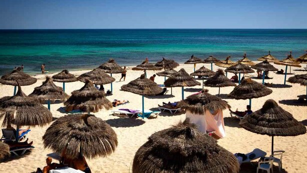 Une plage avec des parasols en chaume et des chaises longues.