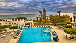 Une piscine avec des chaises longues, une vue sur la mer et des palmiers.