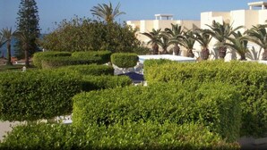 Un espace paysager agrémenté de haies soigneusement taillées, de palmiers et d’un bâtiment doté d’un toit plat et de murs blancs.