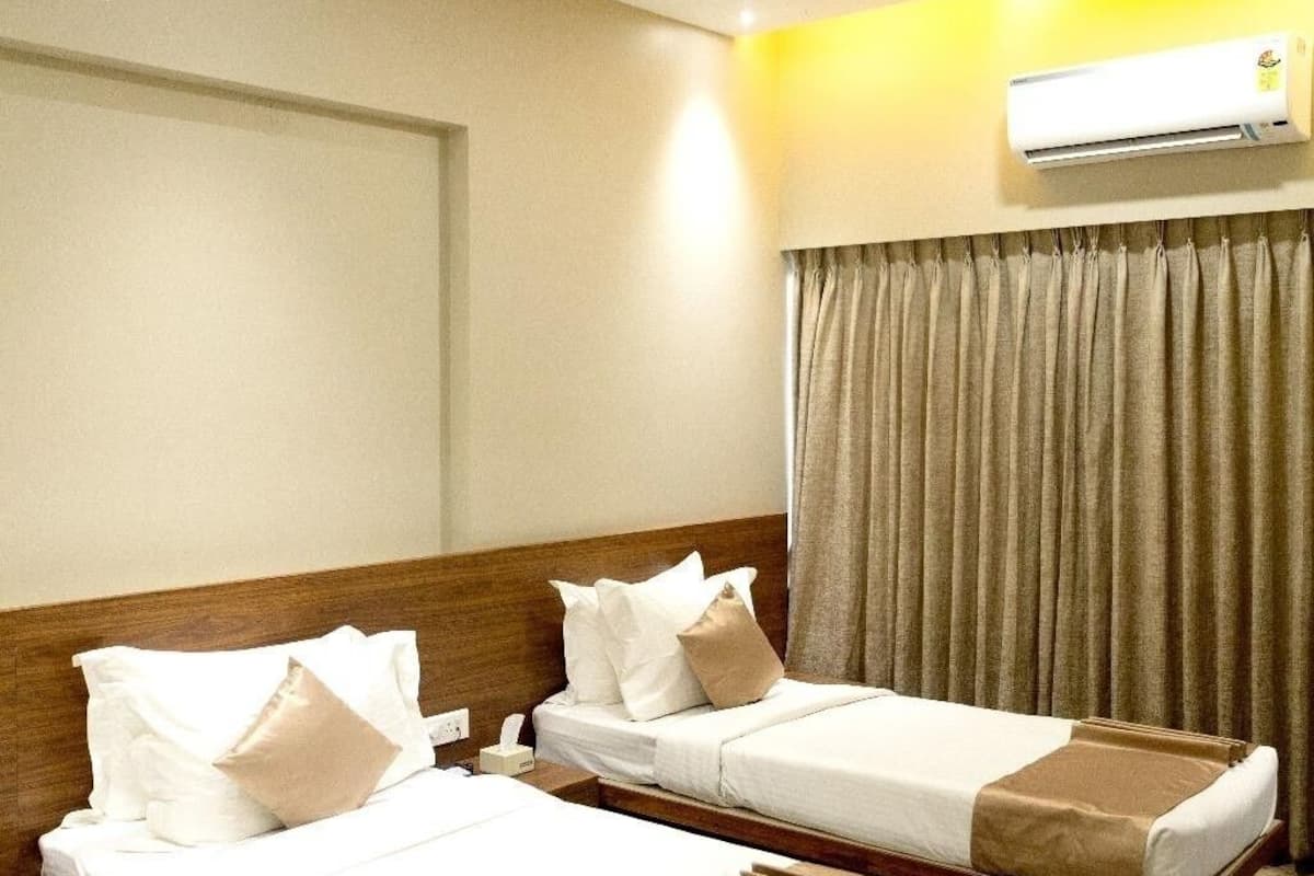 A hotel room with two beds, a ceiling fan, an air conditioning unit, and a window with curtains.