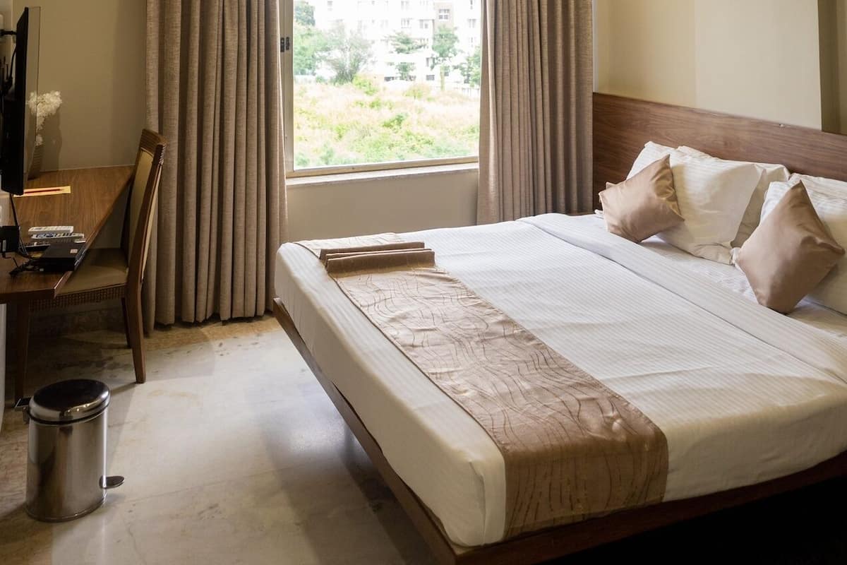 A hotel room with a bed, a desk with a computer, an air conditioner, and a window with curtains.