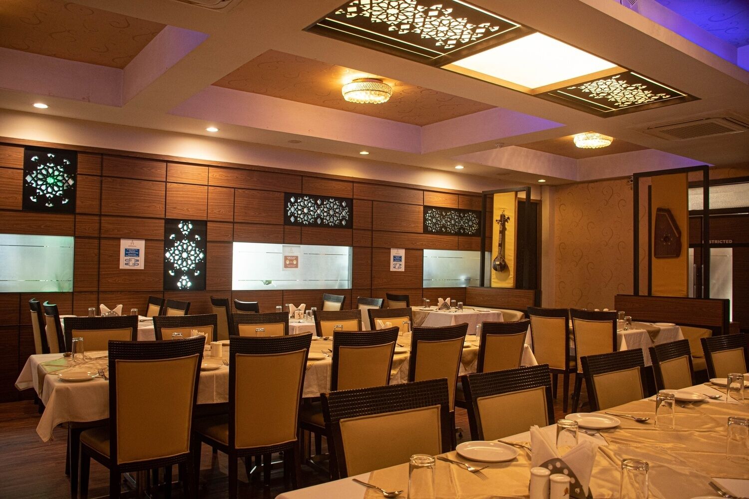 Un salón de banquetes con varias mesas dispuestas para comer, paredes de paneles de madera y lámparas decorativas en el techo.