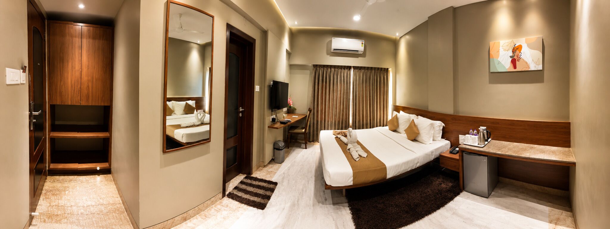 A hotel room with a bed, bedside table, TV, desk, and wardrobe.