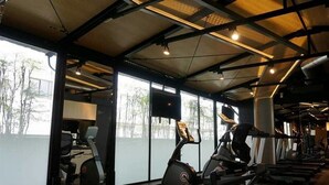 A gym with exercise equipment, large windows, and a view of trees outside. - Gala Hotel (Taipei)