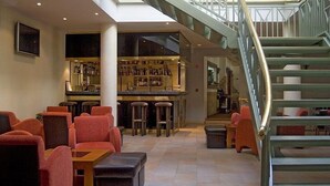 Uma área de bar com banquetas, um balcão e uma escada com grades de metal.