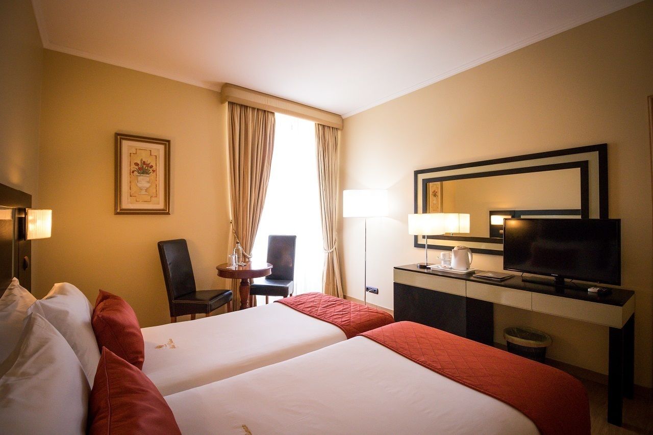 A hotel room with two beds, a desk with a TV, a chair, a lamp, and a framed picture on the wall.