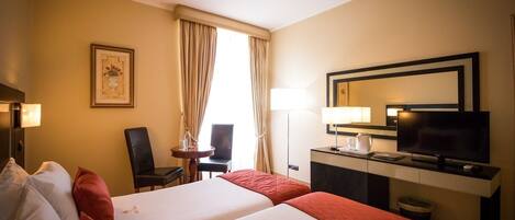 A hotel room with two beds, a desk with a TV, a chair, a lamp, and a framed picture on the wall.