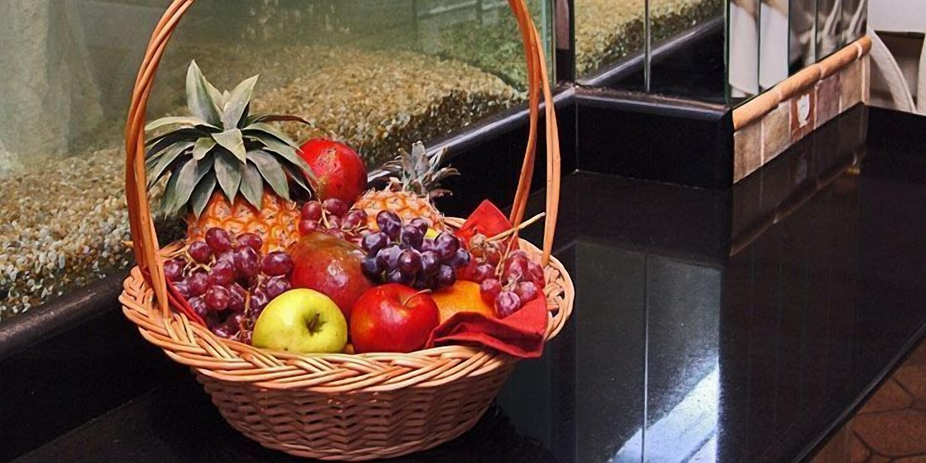 Ein Korankorb, gefüllt mit Obst und Gemüse, auf einer glänzenden schwarzen Oberfläche.
