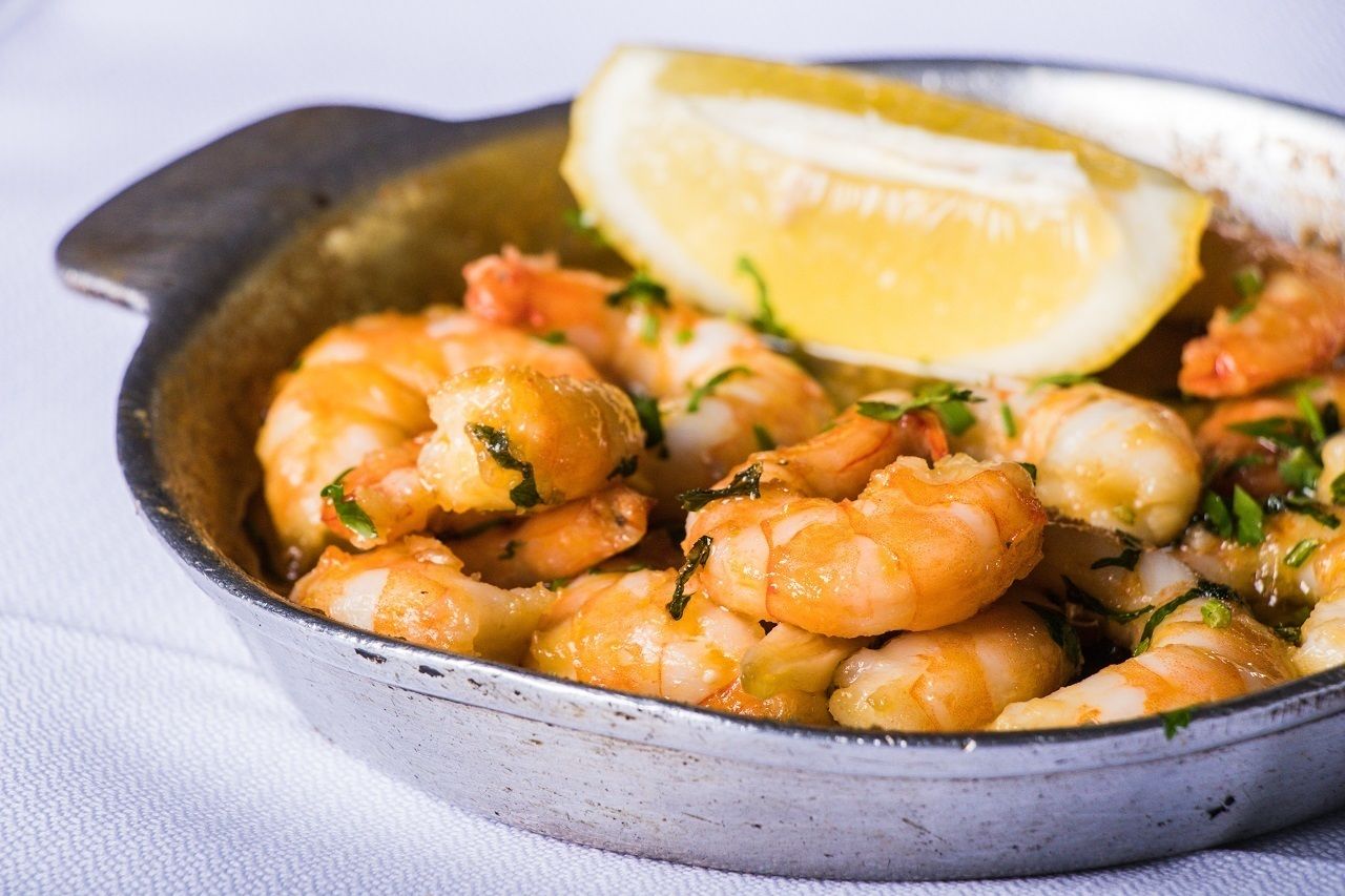 Una sartén con camarones cocidos, adornados con hierbas y un gajo de limón.