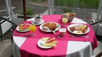 A table set with breakfast items including waffles, eggs, and fruit, with a view of a garden outside.
