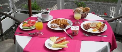 A table set with breakfast items including waffles, eggs, and fruit, with a view of a garden outside.