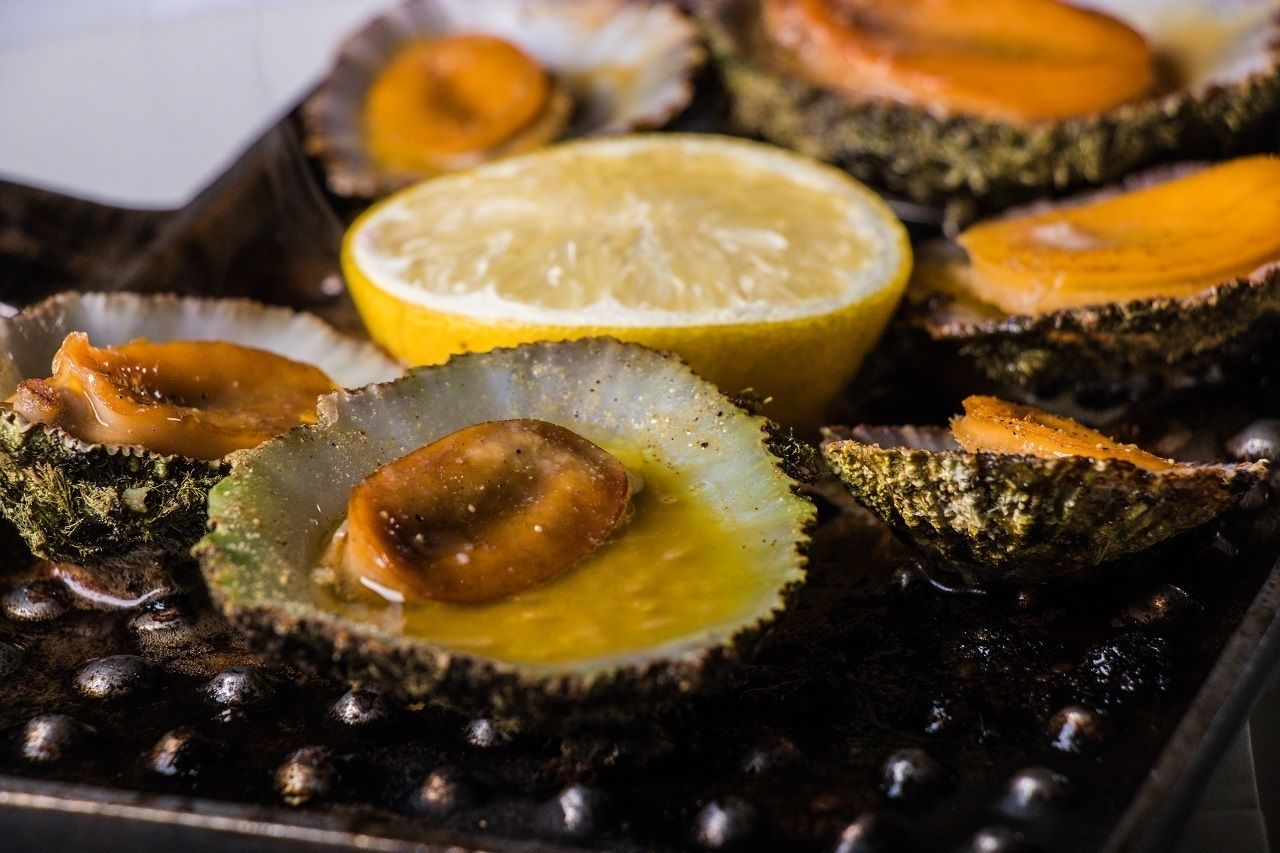 Una bandeja de mariscos a la parrilla, incluyendo ostras y camarones, con cuñas de limón.