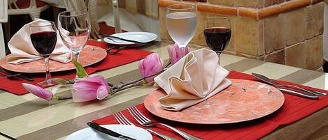 Mesa posta para refeição com pratos, talheres e copos de vinho tinto.