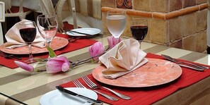 Une table mise pour un repas, avec des assiettes, des couverts et des verres de vin rouge.