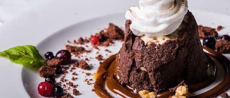 Ein Dessert mit einer Portion Schokoladenkuchen, bedeckt mit Schlagsahne und Karamellsauce, verziert mit Beeren und Walnüssen.