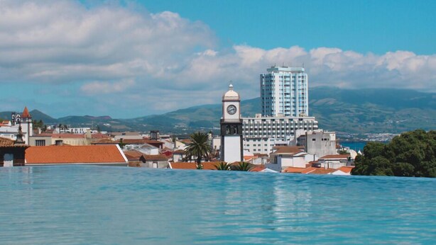 Uma cidade costeira com uma torre do relógio imponente, um edifício moderno e uma vista ampla do mar.