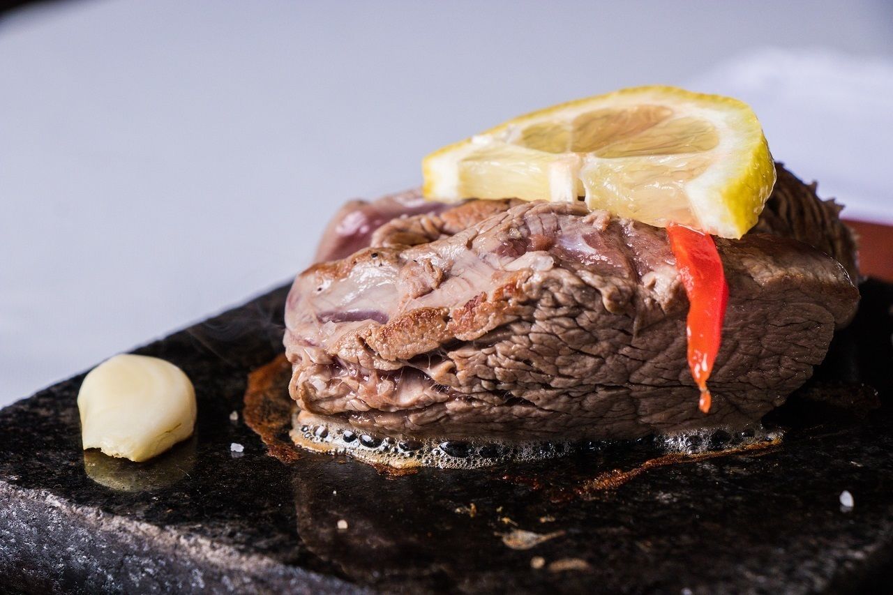 Primer plano de un plato de carne cocida con una rodaja de limón y un chile rojo encima, sobre una superficie oscura.