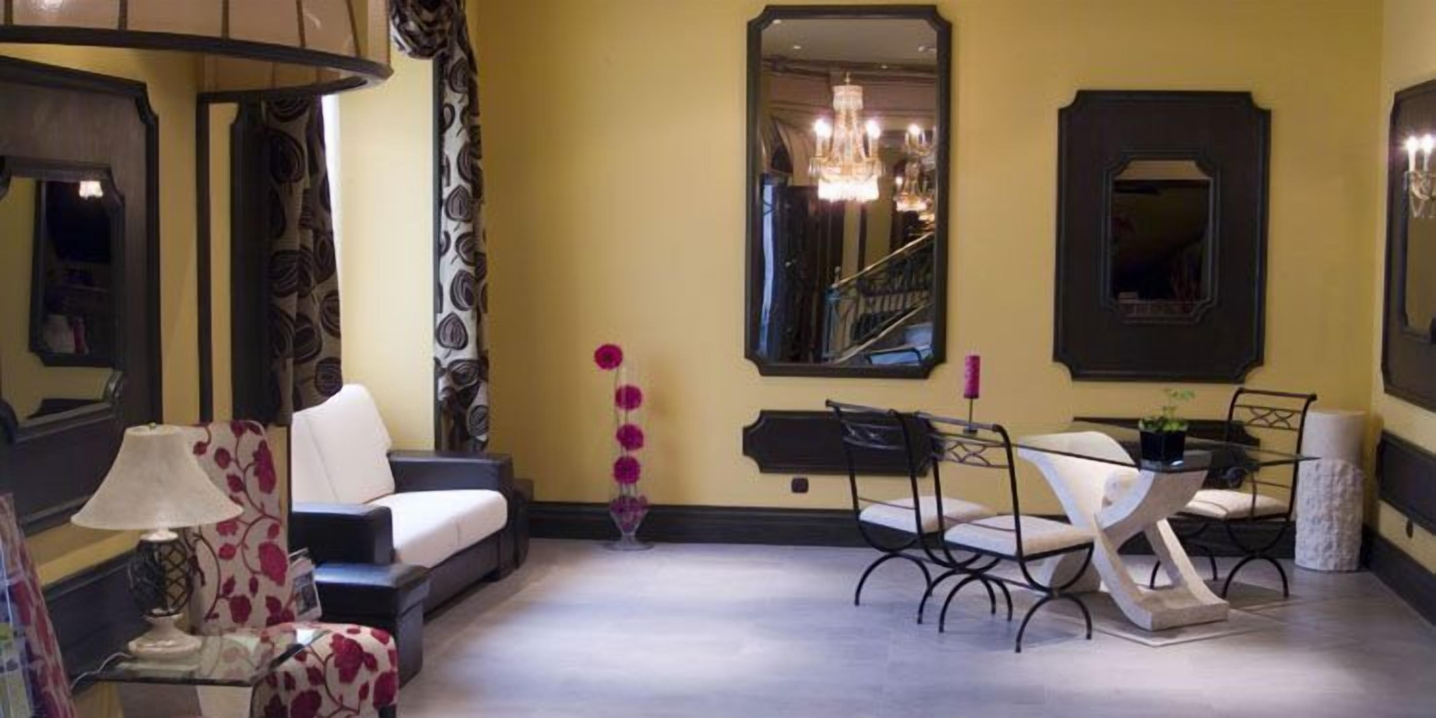 A room with a sofa, a dining table with chairs, a mirror, and a staircase.