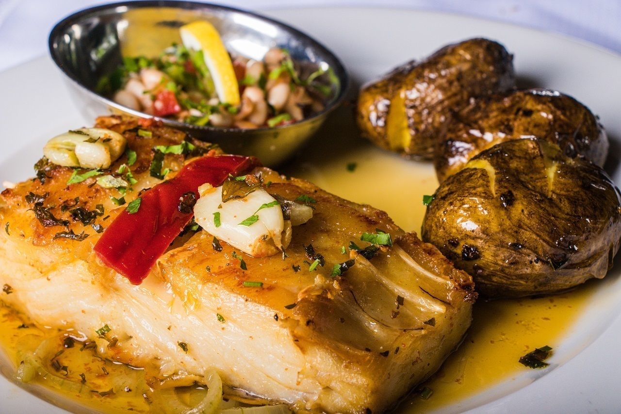 A plate with a piece of fish, roasted potatoes, and a side salad.