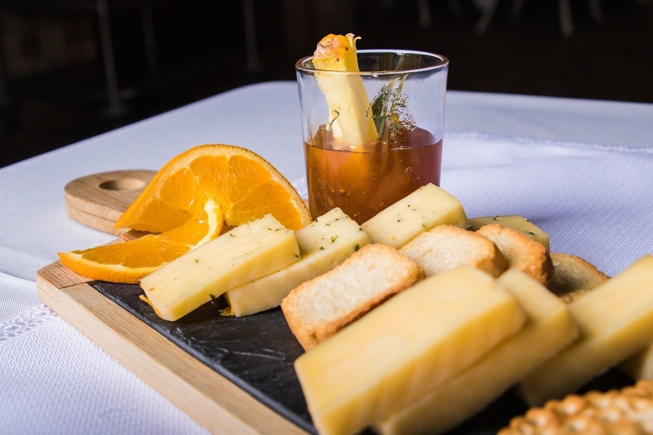 A tray with cheese, bread, and an orange slice on a white tablecloth.