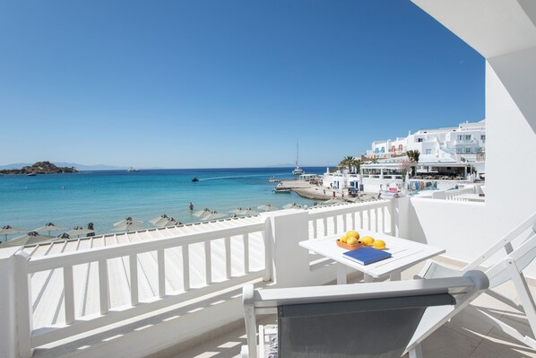 A balcony with a table, chairs, and a view of the sea and buildings. - Acrogiali Beachfront Hotel (Mykonos)