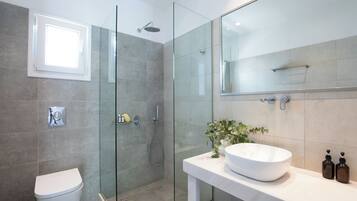 Een moderne badkamer met een glazen douchecabine, een wit toilet en een grote witte wastafel met een bloevas.