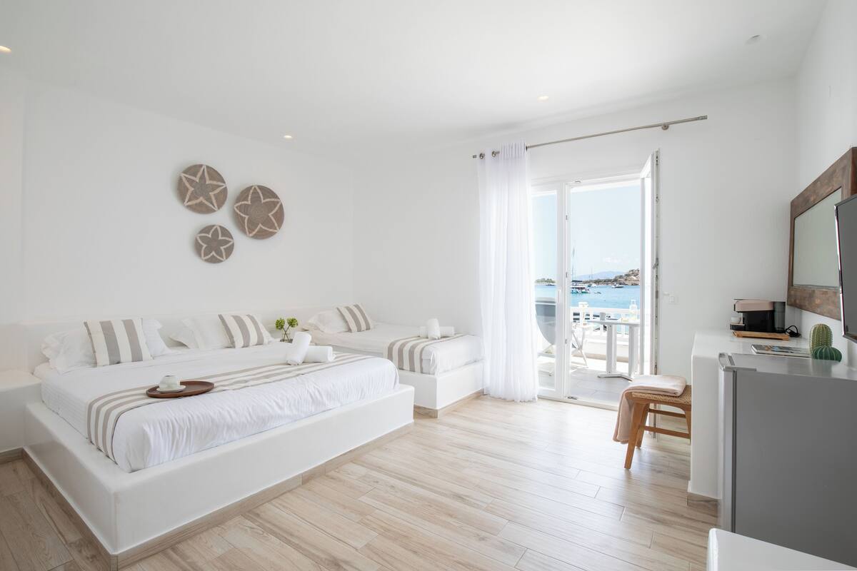 Ein modernes Schlafzimmer mit einem großen Bett, einer kleinen Sitzecke und Meerblick durch eine Schiebetür.