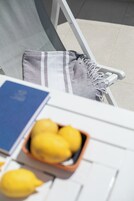 Una silla con un cojín a rayas gris y blanco, un libro azul y un cuenco de limones sobre una mesa blanca.