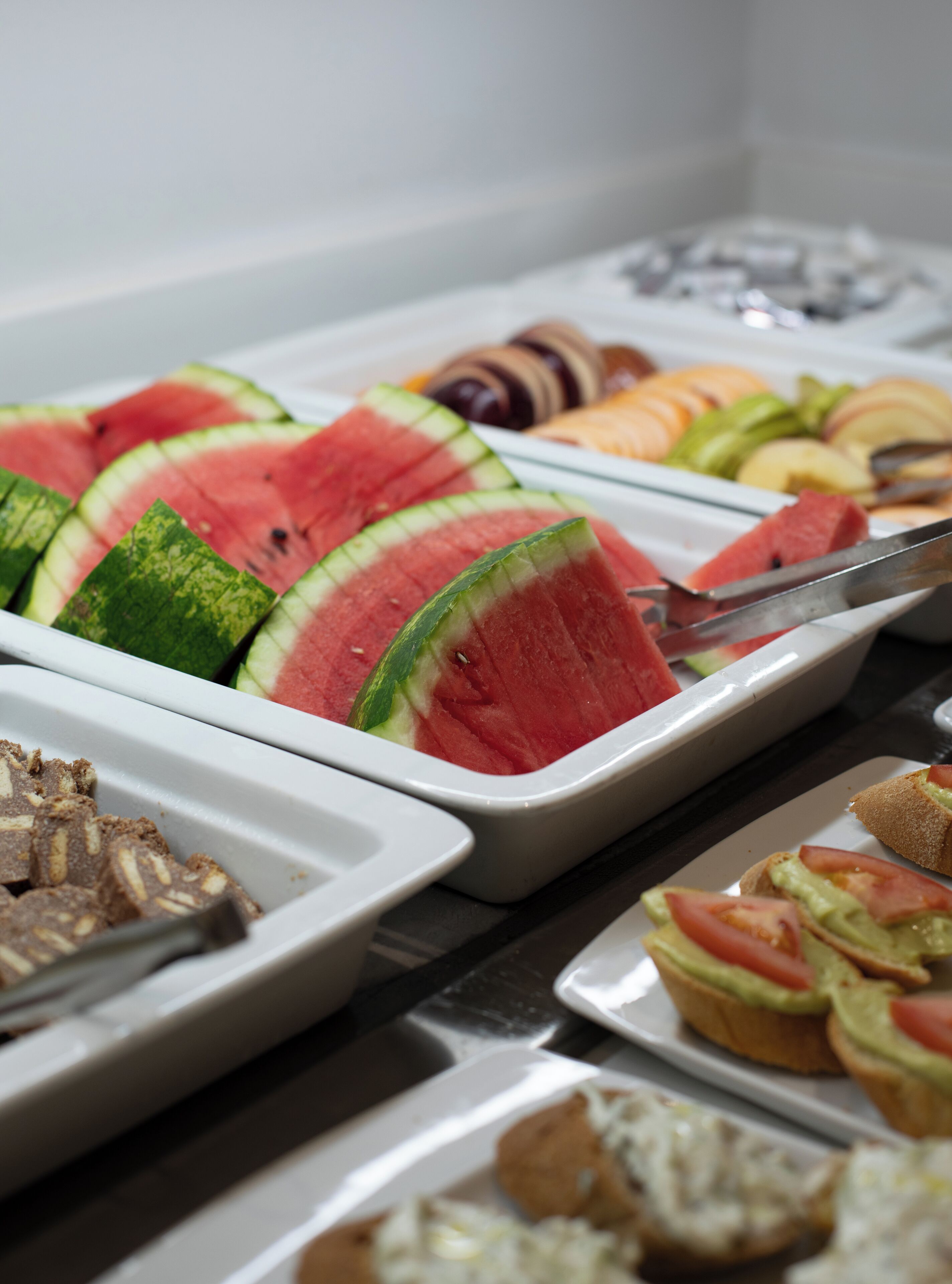 Ein Buffet mit verschiedenen Speisen, darunter Wassermelone, Obst und Sandwiches.