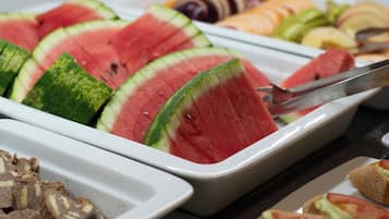 Un bufé con diversas opciones de comida, incluyendo rebanadas de sandía, frutas y sándwiches.