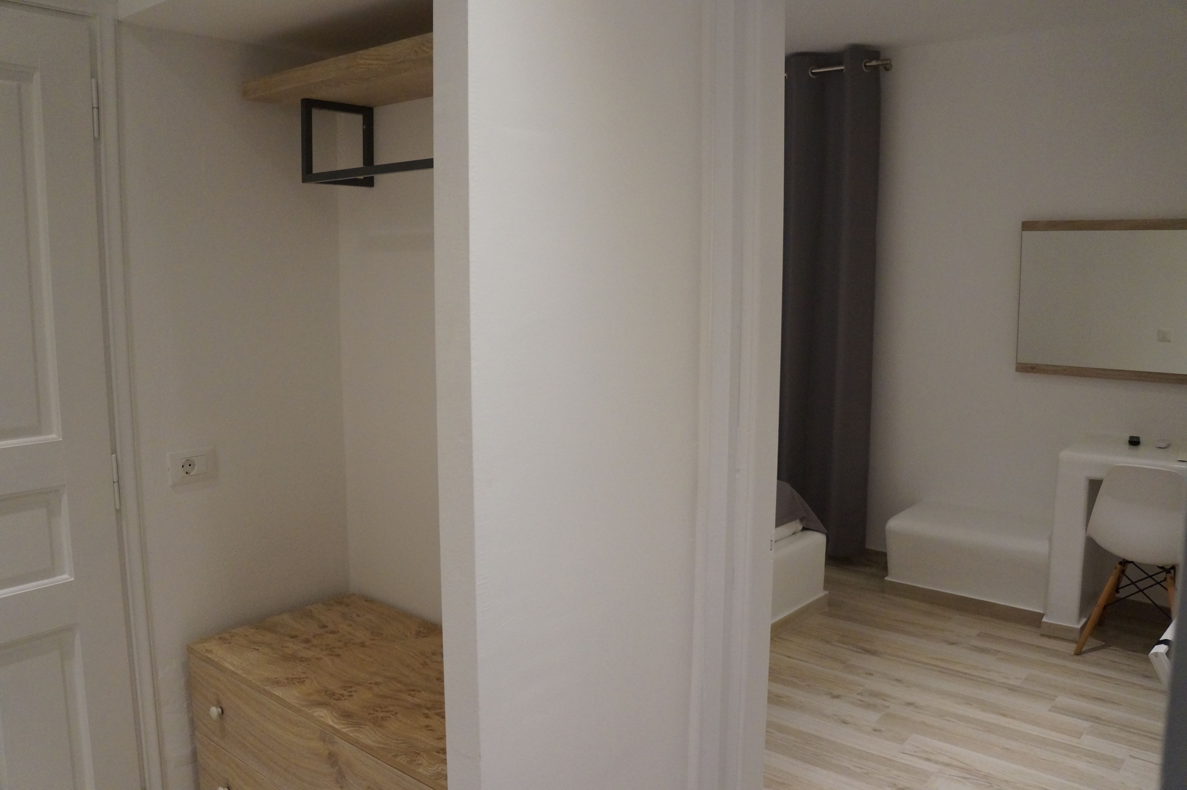 Une pièce comprenant un banc en bois, un bureau blanc, un miroir et un espace douche.