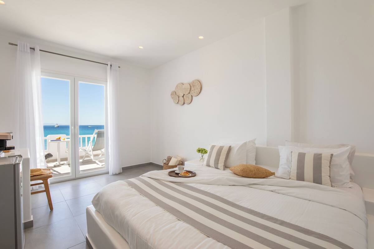 Ein Schlafzimmer mit einem großen Bett, einem Esstisch mit einer Schüssel Essen und Blick auf das Meer durch Glastüren.