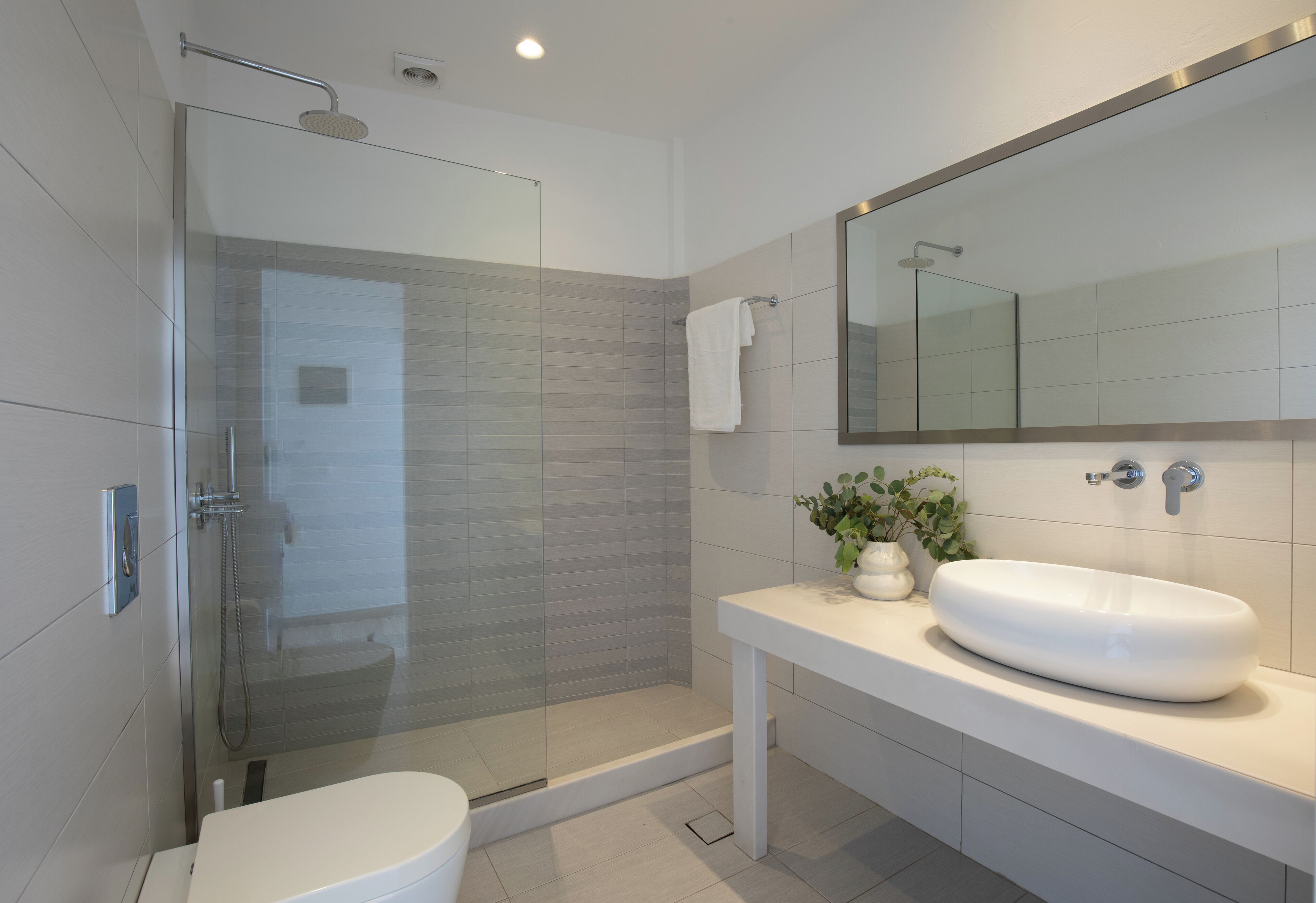 A modern bathroom with a glass-enclosed shower, a white sink, and a large mirror above the vanity.