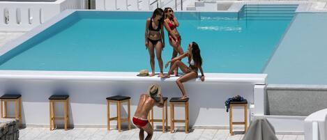 A swimming pool area with sun loungers and a person in swim trunks.