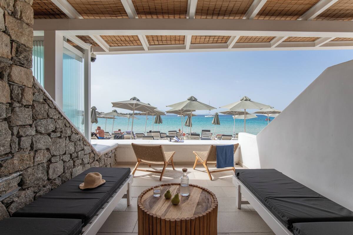 Eine sonnendurchflutete Terrasse mit Steinmauern, Liegestühlen, Sonnenschirmen und Blick auf das Meer.