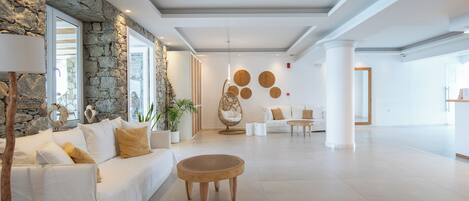 A spacious lobby with a stone wall, a white sofa, a round wooden table, and a decorative wall with circular patterns.