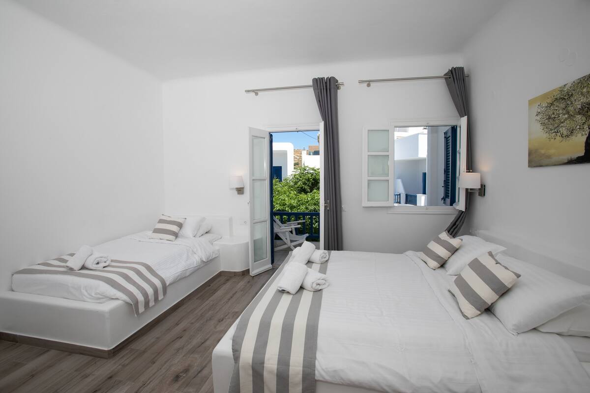 Ein Hotelzimmer mit zwei Betten, einem Balkon und Blick auf Gebäude und Grünflächen.