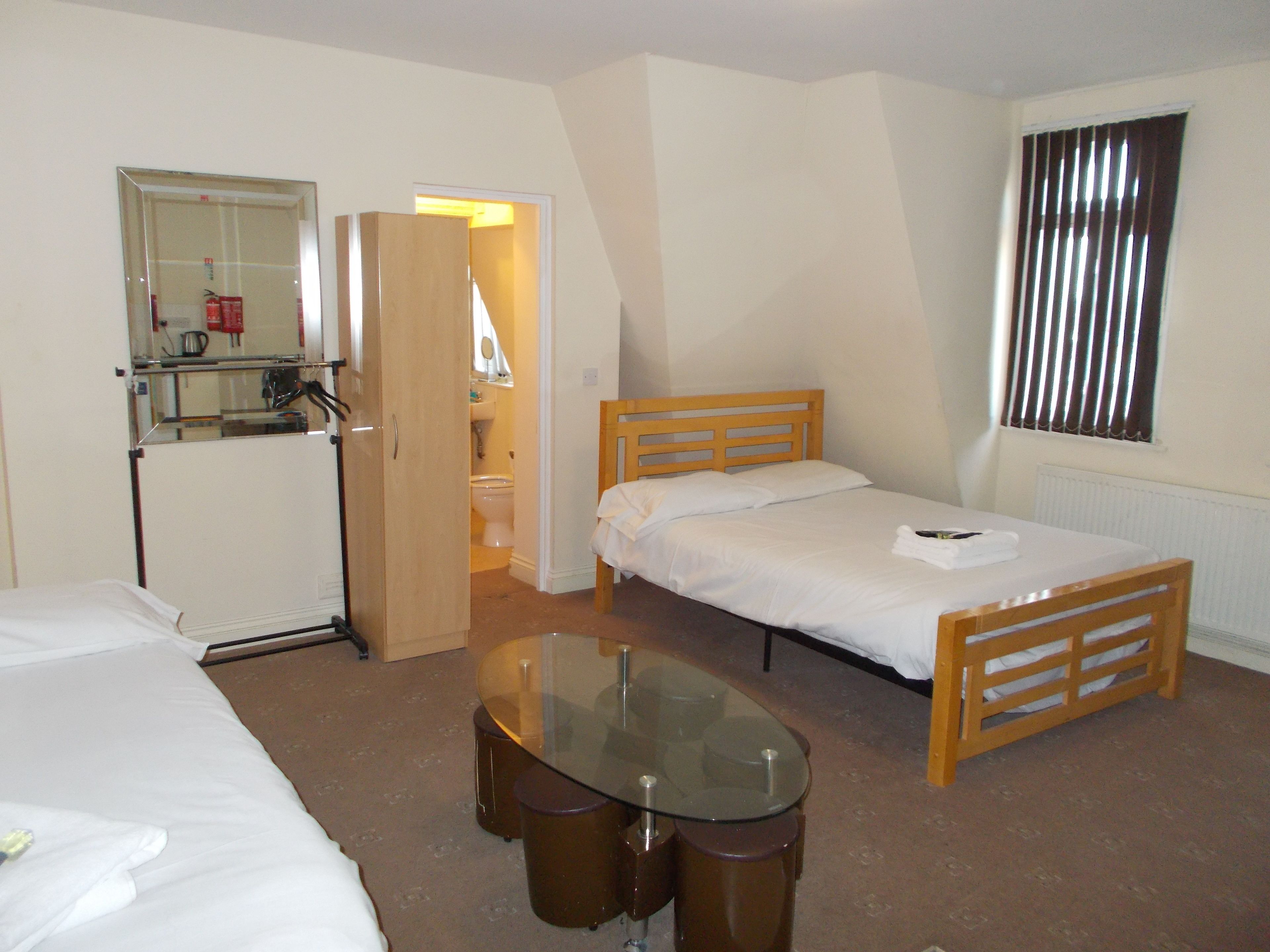 A hotel room with a bed, a small table, a mirror, and a window with blinds.