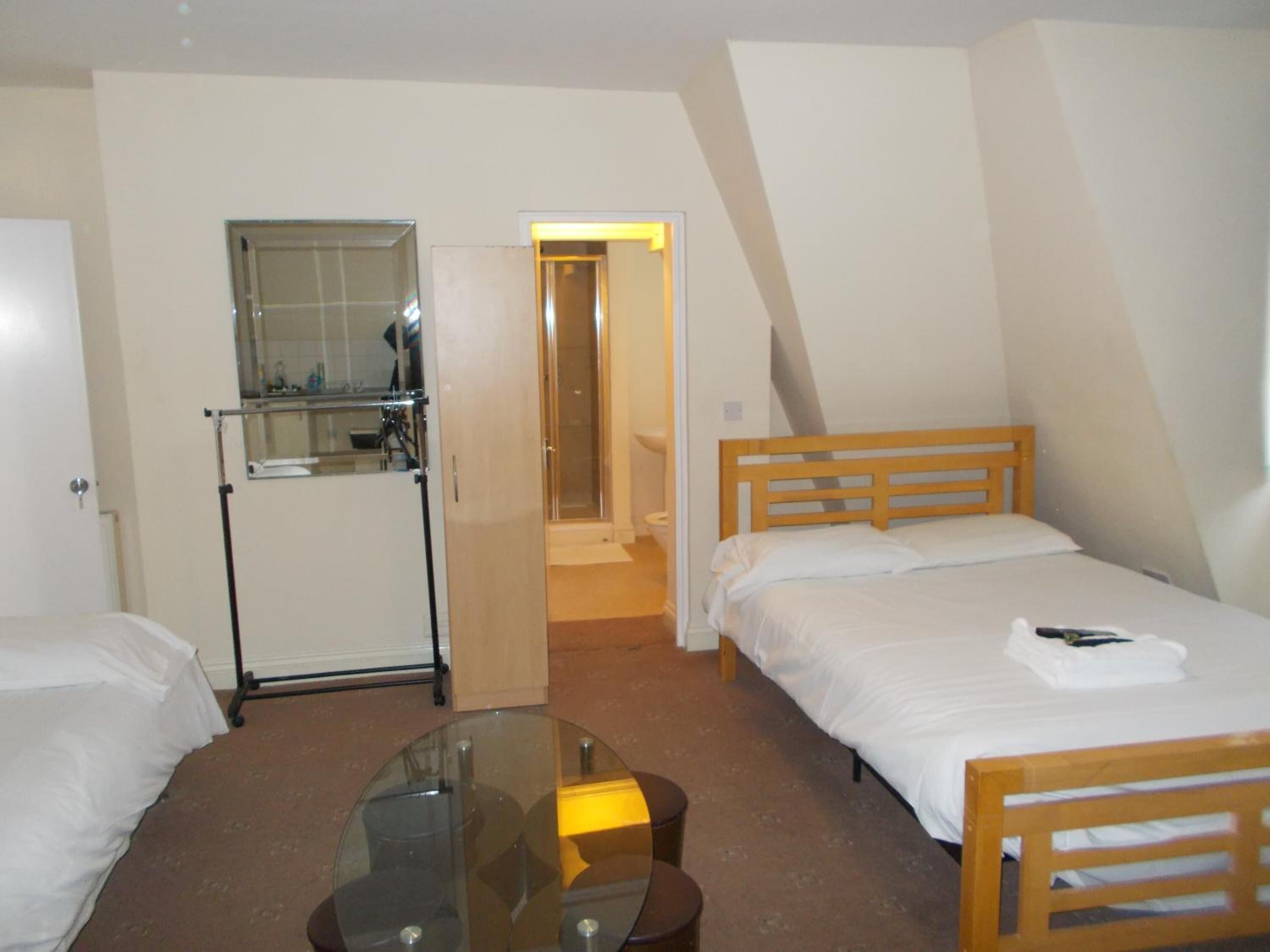 A small, single-room hotel bedroom with a bed, a small table, and a mirror.