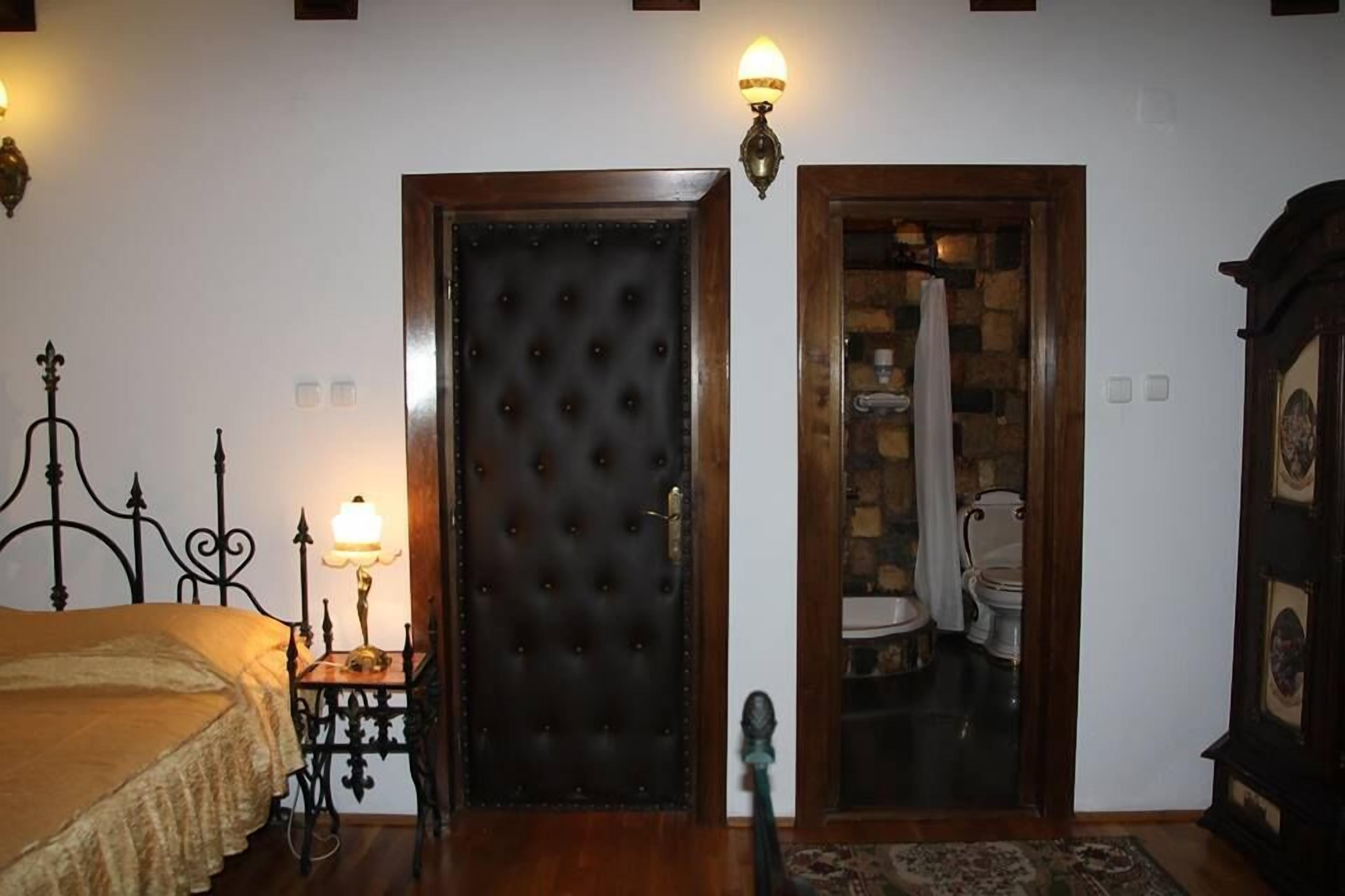 A bedroom with a bed, bedside table, lamp, and a door leading to a bathroom with a toilet and shower.